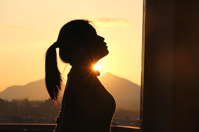 夕日を浴びて上を見上げるポニーテールの少女。